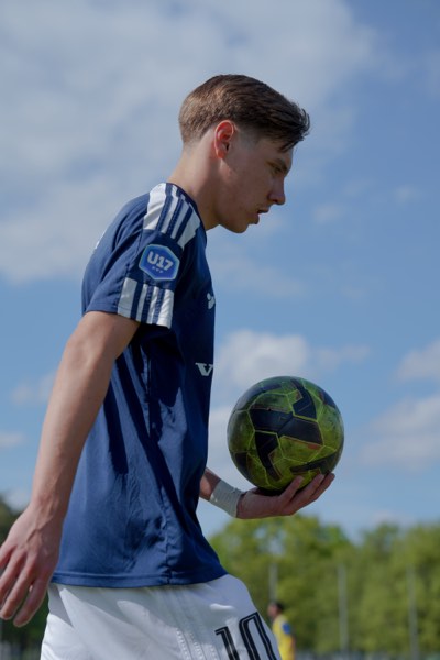 Joueur U17 de profil tenant un ballon, ciel bleu en fond